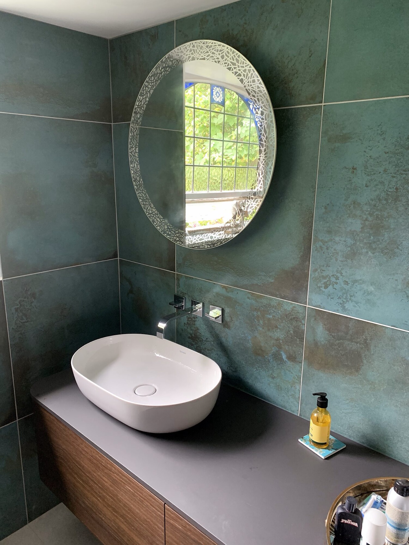 Green metallic tiles with a round lit mirror