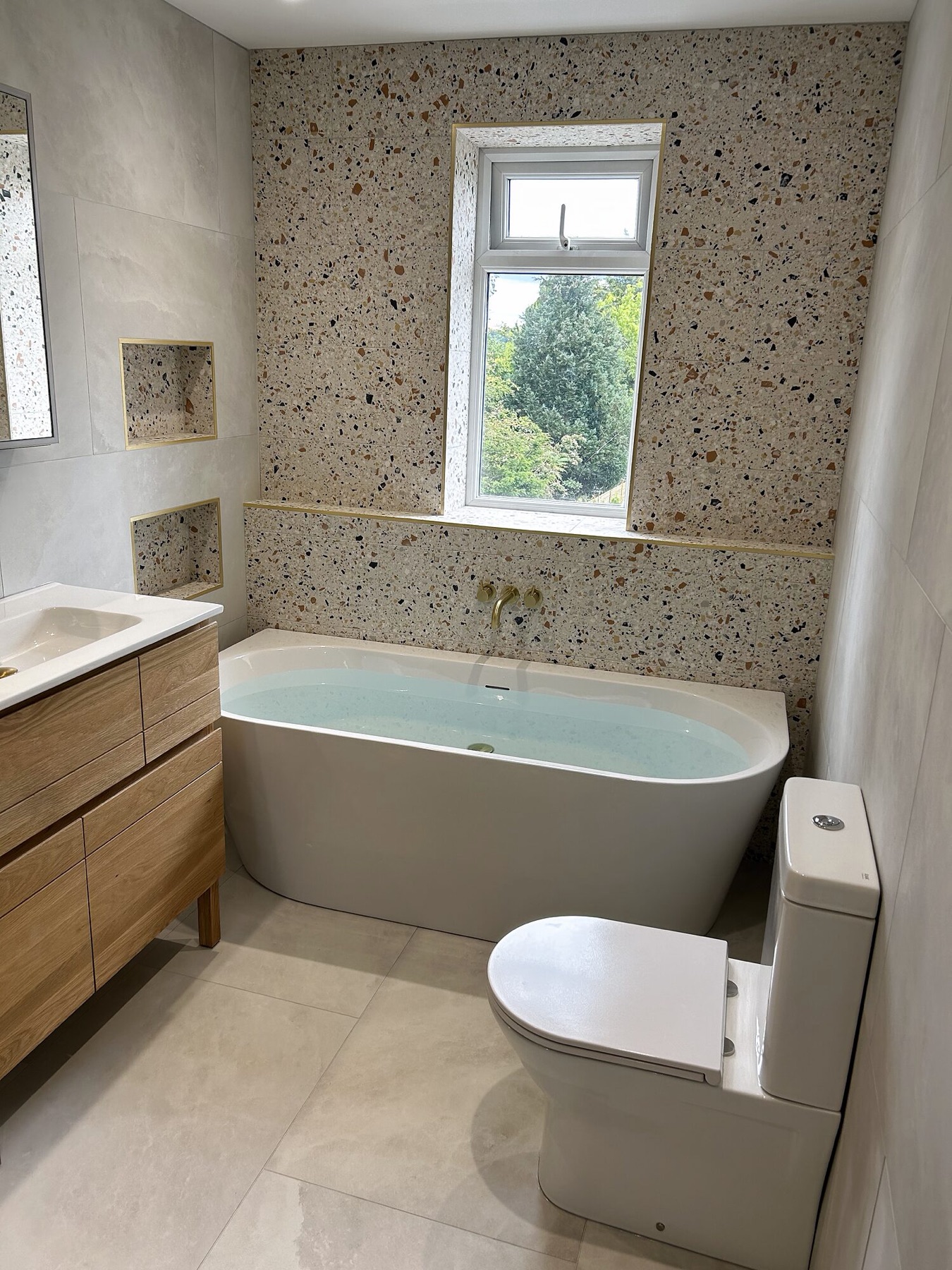 Terrazzo feature wall with a recessed niche and an oak vanity.