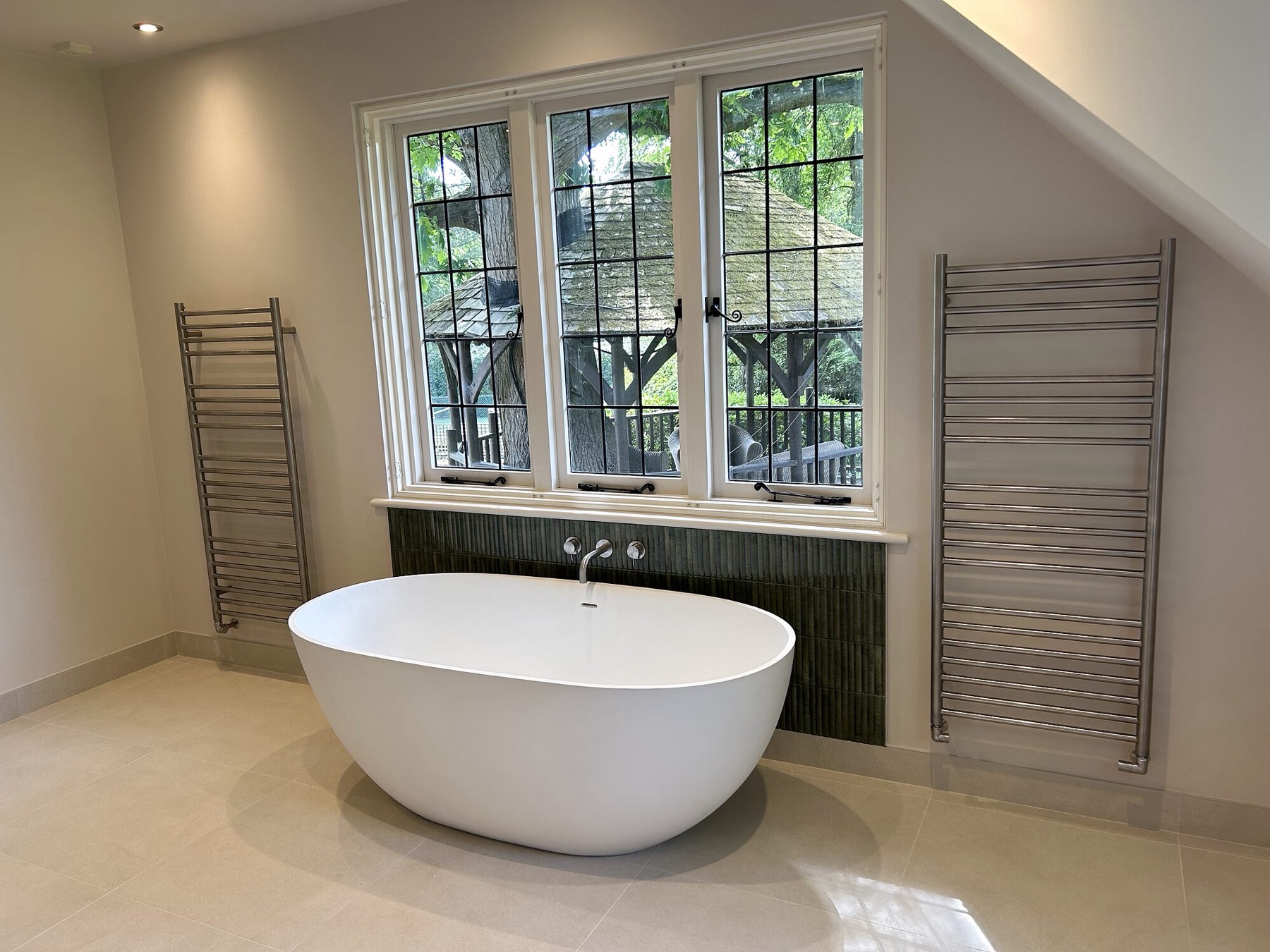 Freestanding bath under leaded windows, with tall heated towel rails.